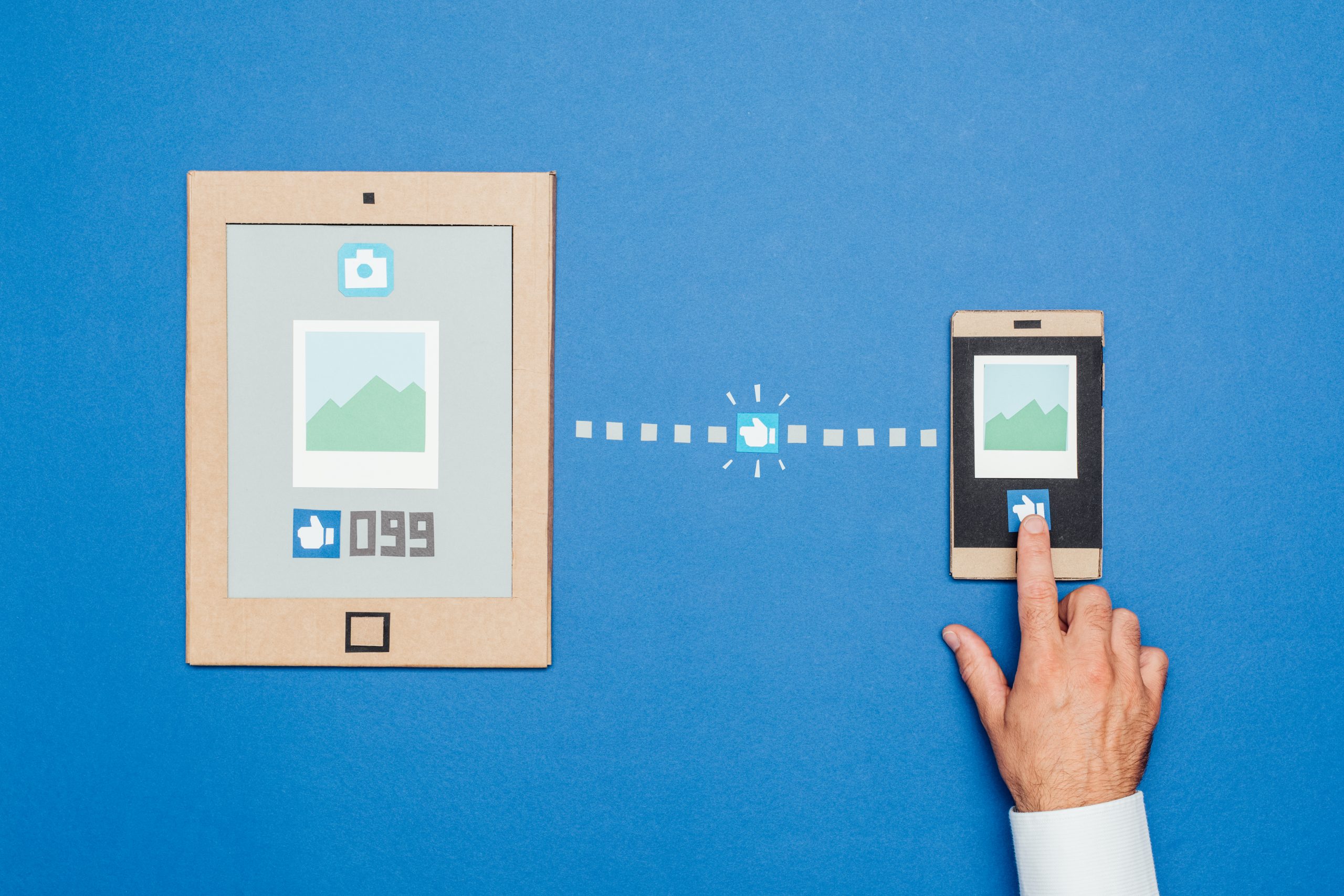 Social media and content sharing: an user is giving a like to a picture using a smartphone; handmade devices made from recycled cardboard